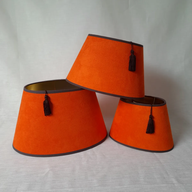 The Hermès 20 cm oval and conical lampshade is suitable for all types of lamp bases. The exterior is in orange suede, while the interior is gold, diffusing a warm, radiant light into the room.